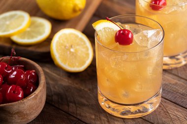 Whiskey sour cocktail with marachino cherry and lemon slice on rustic wooden table