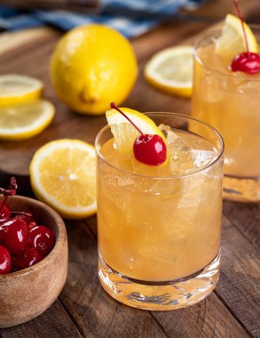 Whiskey sour cocktail with marachino cherry and lemon slice on rustic wooden table