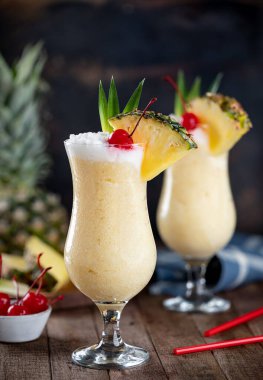 Pina colada cocktail garnished with cherry, pineapple slice and leaves on a rustic wooden table