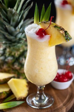 Pina colada cocktail garnished with cherry, pineapple slice and leaves on a wooden platter
