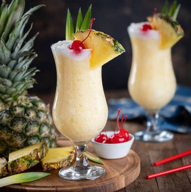 Pina colada cocktail garnished with cherry, pineapple slice and leaves on a wooden platter
