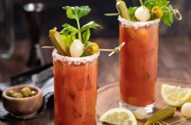 Kanlı Mary kokteyli kereviz, bamya, soğan, zeytin ve tuzla süslenmiş koyu ahşap bir arka planda.