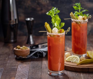 Kanlı Mary kokteyli kereviz, bamya, soğan, zeytin ve tuzla süslenmiş koyu ahşap bir arka planda.