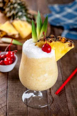 Vişneli, ananas dilimli Pina colada kokteyli ve kırsal ahşap bir masada yapraklar.
