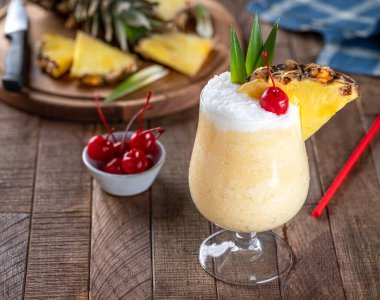 Vişneli, ananas dilimli Pina colada kokteyli ve kırsal ahşap bir masada yapraklar.