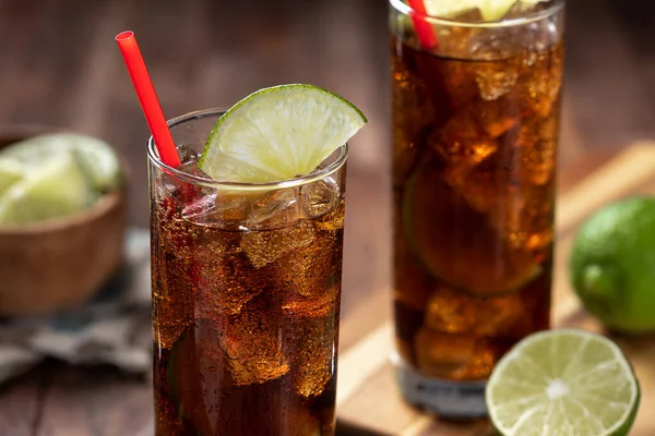 stock image Rum and cola cocktail in tall glasses with lime slice on rustic wooden table