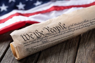 United States constitution with American flag in background on rustic wooden table clipart
