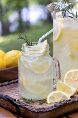 Limon dilimleri ve ahşap tepside biberiyeli bir sürahi limonata.