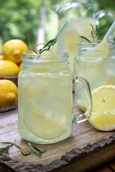 Limonata, dilimlenmiş limonlar, biberiye ve buz ile ahşap bir tepside iki cam kavanozda.