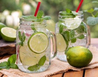 Limon dilimli mojito kokteyli ve doğa arka planlı ahşap masada nane şekeri.