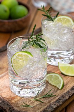 Limon dilimleri ve ahşap tepside biberiye ile süslenmiş cin ve tonik kokteyl.