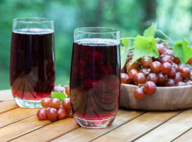 Üzüm suyu bardakta kırmızı üzümlü ahşap veranda masasında, arka planda kırmızı üzümlü.