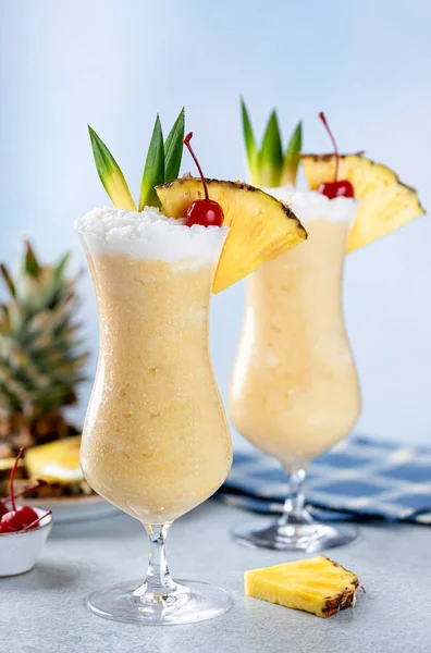 Pina colada cocktails with cherry, pineapple slice and leaves on a blue background