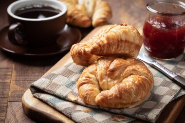 Çilek reçelli iki kruvasan ve kırsal ahşap masada bir fincan kahve.