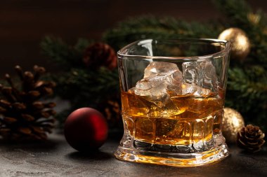 Glass of whiskey with ice on wooden surface and Christmas decorations in background clipart