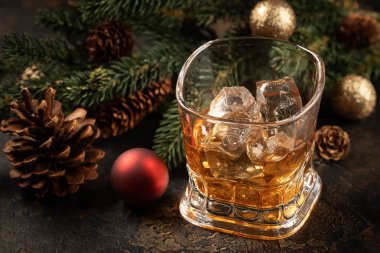 Ahşap yüzeyde bir bardak viski ve buz. Arka planda Noel süsleri var.