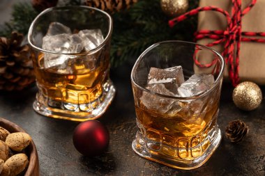 Arka planda Noel süsleri olan ahşap yüzeyde iki bardak viski ve buz.