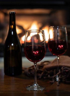 Battaniyeli iki kadeh kırmızı şarap ve ahşap masa. Bqckground 'da şömine yakılıyor