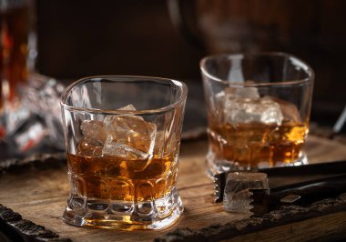 Kırsal ahşap tepside buzlu iki bardak viski ve arka planda sürahi.