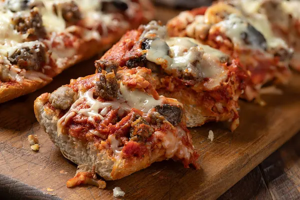 Closeup of pizza bread made with sausage, mozzarella cheese and tomato sause sliced on an old wooden cutting board