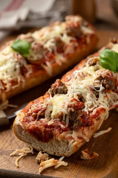 Pizza bread made with sausage, mozzarella cheese and tomato sause on an old wooden cutting board