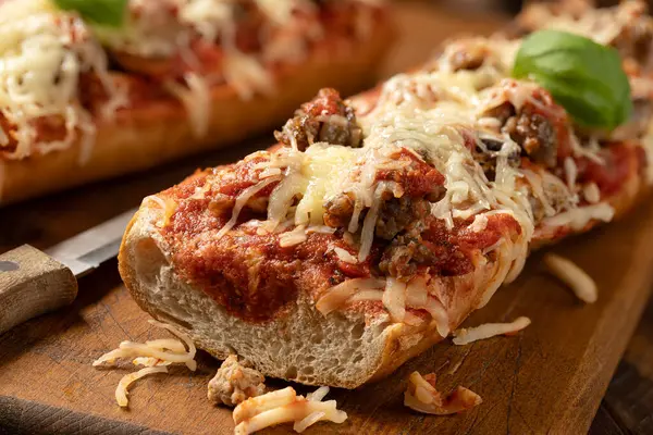 Closeup of pizza bread made with sausage, mozzarella cheese and tomato sause on an old wooden cutting board