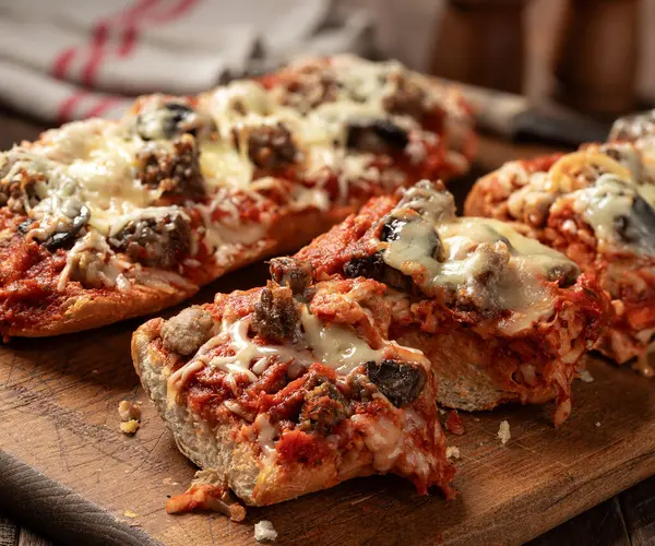 Pizza bread made with sausage, mozzarella cheese and tomato sause sliced on an old wooden cutting board