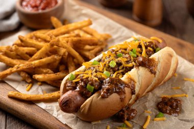 Biberli sosisli, dilimlenmiş çedar peyniri ve ahşap bir tahtanın üzerinde patates kızartması.