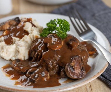 Maydanozla süslenmiş mantar soslu Salisbury bifteği ve beyaz tabakta patates püresi.