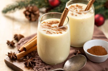 İki bardak tarçınlı yumurta likörü ve arka planda tatil süsleri olan ahşap masa üzerinde anason.