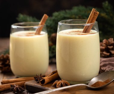 İki bardak tarçınlı yumurta likörü ve arka planda tatil süsleri olan ahşap masa üzerinde anason.