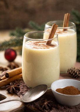 İki bardak tarçınlı yumurta likörü ve arka planda tatil süsleri olan ahşap masa üzerinde anason.