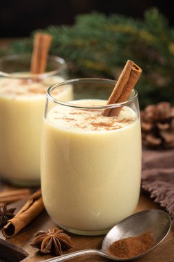 İki bardak tarçınlı yumurta likörü ve arka planda tatil süsleri olan ahşap masa üzerinde anason.