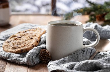 Steaming cup of coffee and blanket by a window with snowy winter background clipart