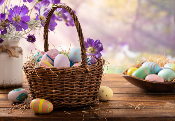 Пасхальные яйца в корзине и фиолетовые маргаритки на деревянном столе с ярким весенним фоном