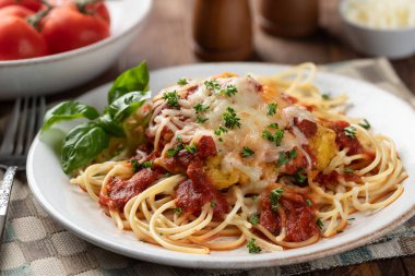 Makarna ve fesleğen yapraklarıyla süslenmiş soslu parmesanlı tavuk ve akşam yemeği tabağında maydanoz.