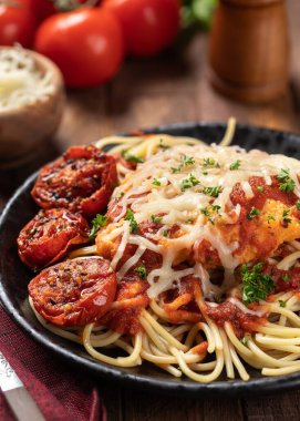 Makarnalı parmesanlı tavuk, sos ve fesleğen yapraklarıyla süslenmiş kızarmış domates ve akşam yemeği tabağında doğranmış maydanoz.