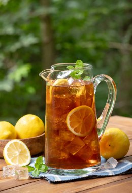 Limon dilimli bir sürahi buzlu çay ve doğa arka planlı ahşap bir masada naneli şeker.