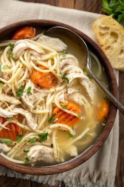 Bir kase tavuklu şehriye çorbası, peçetede havuç ve tahta masada baget dilimleri. Genel Görünüm