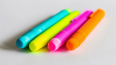 Dört parlak renkli fosforlu kalem mavi, sarı, pembe ve turuncu, beyaz arka planda yan yana dizilmiş..