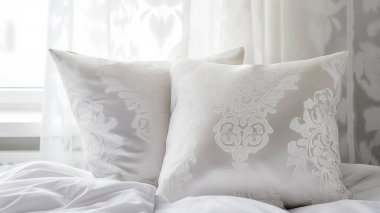 Karmaşık desenli iki zarif beyaz yastık, rahat ve davetkar bir yatak odası ortamı yaratıyor..