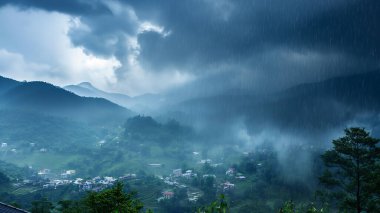 Bulutlu bir gökyüzünün altındaki puslu dağlar karamsar, atmosferik bir manzara yaratıyor..