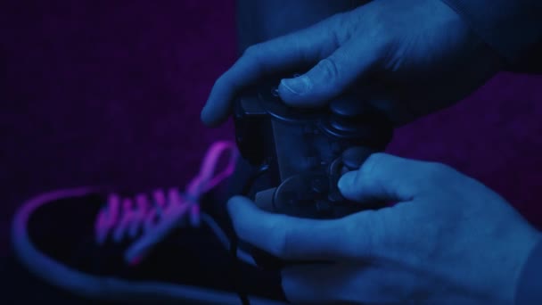 一个视频游戏玩家在一个没有品牌的通用游戏控制器上的按钮上快速移动着拇指和锤子 只有粉色和蓝色闪烁的电视屏幕照亮了它 — 图库视频影像
