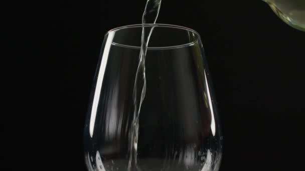 白ワインは完全に黒い背景に対して大きなワイングラスに注がれます ワインはスプラッシュとドリップで素早く注ぎ込まれ ワインは気泡によって落ち着くように曇ります — ストック動画