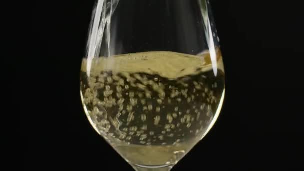 白葡萄酒倒入一个大酒杯中 其背景完全是黑色的 酒很快被水花和水滴倾泻而下 当它沉淀下来的时候 被气泡蒙上了一层云彩 — 图库视频影像