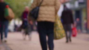 Bokeh 'te yayalar ve müşterilerle dolu şehir merkezi caddesi. İngiltere 'de şehir dolandırıcılığının ve ticari perakende faaliyetlerinin spesifik olmayan temsili. Şehir koşuşturması ve ticari faaliyet için spesifik olmayan temsiller gerektiren projeler için ideal.