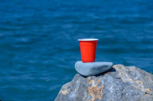 Rotes Plastikglas Auf Dem Hintergrund Des Meeres Und Des Strandes — Stockfoto