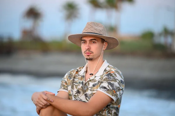 a young guy with a mustache and a hat  on a stone on the shore of the Mediterranean Sea 1