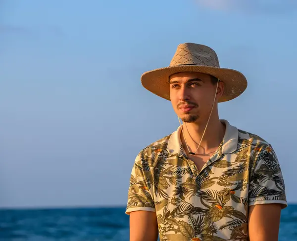 a young guy with a mustache and a hat sits on a stone on the shore of the Mediterranean Sea 12