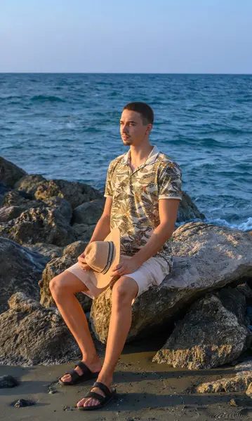 a young guy with a mustache and sits on a stone on the shore of the Mediterranean Sea 1